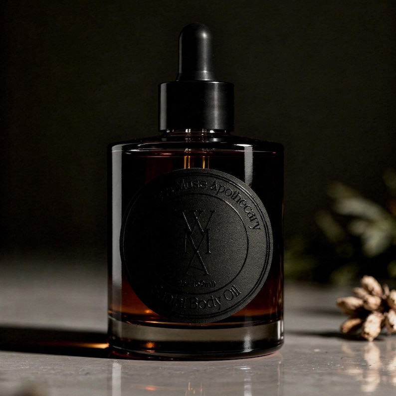 May include: A cylindrical amber glass bottle with a black dropper cap. A circular black label on the front features the text Wild Muse Apothecary, WMA, and 2oz (59ml) Ritual Body Oil. The bottle contains a dark liquid and has a flat base.