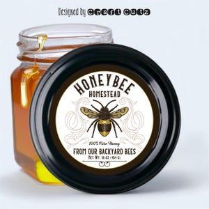 May include: A round honey jar label with a black background and white text. The label features a stylized illustration of a honeybee with gold accents. The text reads "Honeybee Homestead 100% Pure Honey From Our Backyard Bees Net Wt. 16 oz (454 g)"