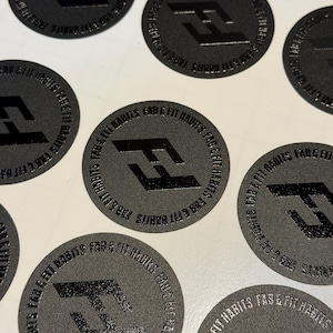 May include: A collection of circular black stickers featuring a glossy black logo of the letters FF in the center. The text FAB & FIT HABITS is printed in a circular pattern around the logo. The stickers have a matte, textured finish.