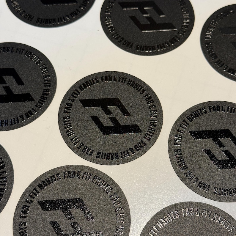 May include: A collection of circular black stickers featuring a glossy black logo of the letters FF in the center. The text FAB & FIT HABITS is printed in a circular pattern around the logo. The stickers have a matte, textured finish.
