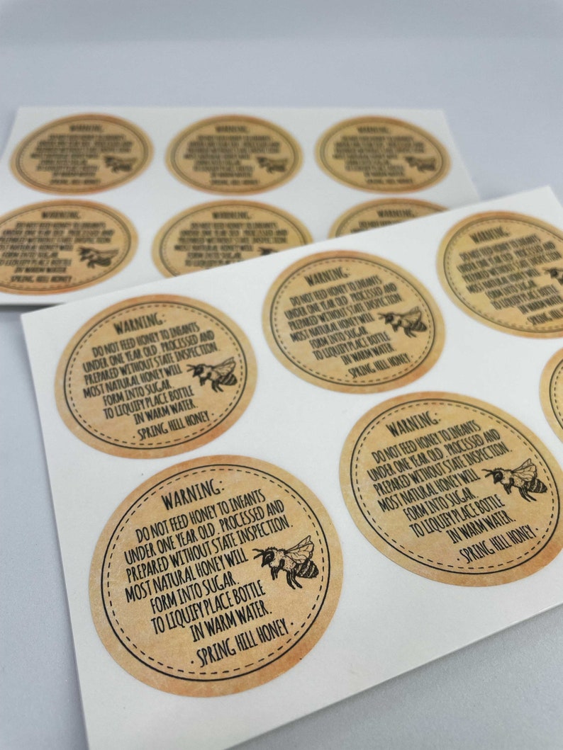 Peut inclure: Une feuille d'&eacute;tiquettes en papier brun avec un avertissement concernant l'alimentation des nourrissons de moins d'un an avec du miel. Les &eacute;tiquettes pr&eacute;sentent une illustration d'abeille et le texte "AVERTISSEMENT : NE PAS DONNER DE MIEL AUX BEBES DE MOINS D'UN AN. TRAITE ET PREPARE SANS INSPECTION DE L'ETAT. LA PLUPART DU MIEL NATUREL SE TRANSFORMERA EN SUCRE. POUR LIQUEFIER, PLACER LA BOUTEILLE DANS DE L'EAU CHAUDE. MIEL DE SPRING HILL."