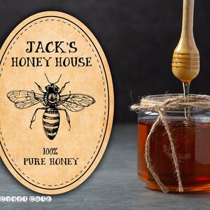 Peut inclure: Une &eacute;tiquette de miel de style vintage avec le texte "Jack's Honey House" et un dessin d'une abeille. L'&eacute;tiquette est sur un fond beige avec une bordure brune et le texte "100% Pure Honey".