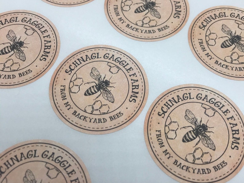 Peut inclure: Cinq &eacute;tiquettes rondes en papier brun avec du texte noir et une illustration d'abeille. Le texte sur les &eacute;tiquettes indique "Schnagl Gaggle Farms" et "From My Backyard Bees".