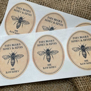 Peut inclure: Quatre &eacute;tiquettes rondes en papier brun avec une illustration d'abeille noire et le texte "Papa Bear's Honey & Hives" et "100% Raw Honey".