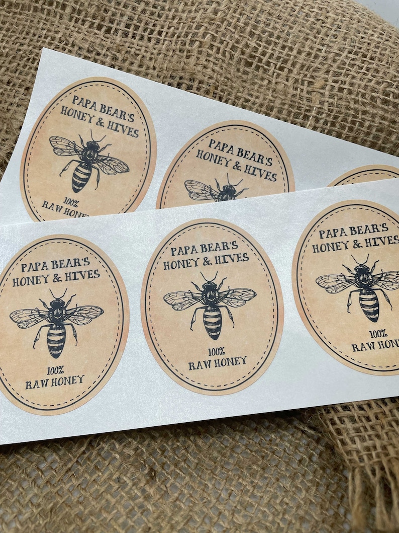Peut inclure: Quatre &eacute;tiquettes rondes en papier brun avec une illustration d'abeille noire et le texte "Papa Bear's Honey & Hives" et "100% Raw Honey".