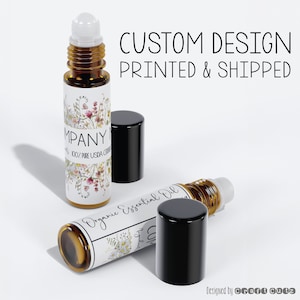May include: Two amber glass roller bottles with black caps. The bottles are labeled with white labels featuring a floral design and the text "Organic Essential Oil" and "Company Name 100% Pure USDA Certified". The text "Custom Design Printed & Shipped" appears above the bottles.