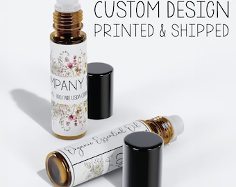 May include: Two amber glass roller bottles with black caps. The bottles are labeled with white labels featuring a floral design and the text "Organic Essential Oil" and "Company Name 100% Pure USDA Certified". The text "Custom Design Printed & Shipped" appears above the bottles.