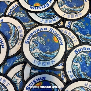May include: Circular patches with a blue and white wave design, the text "SHIDOKAN SEISHIN" and Japanese characters. The patches have a black border and are scattered across a surface.