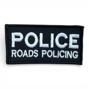 May include: A black rectangular patch with white embroidered lettering. The text reads "POLICE" above "ROADS POLICING". The patch has a black border and is likely for police or security personnel.