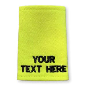 May include: A vivid yellow rectangular patch featuring the embroidered words "YOUR TEXT HERE" in black. The patch is made of woven fabric and has a stitched border.