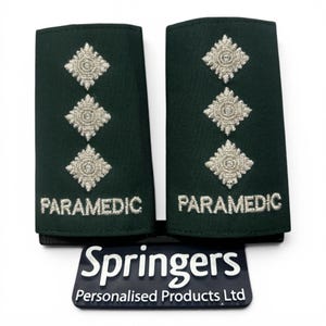 May include: A pair of dark green rectangular epaulettes featuring three embroidered silver diamond-shaped pips and the word PARAMEDIC in silver thread. Below the epaulettes is a black rectangular sign with the text Springers Personalised Products Ltd.