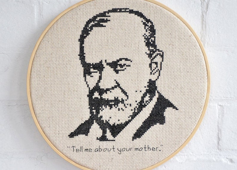 May include: Black and white cross-stitch embroidery of a man's face with a quote, "Tell me about your mother."