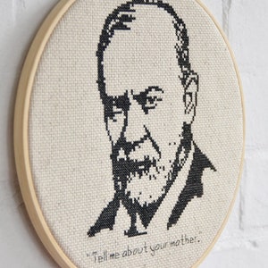 May include: A black and white cross-stitch embroidery of a man's face with a beard and the quote "Tell me about your mother." The embroidery is framed in a wooden hoop.