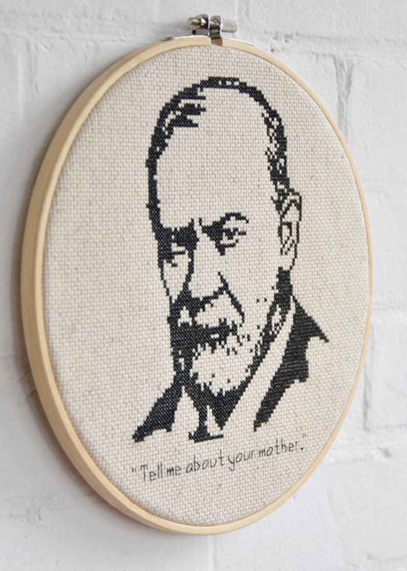 May include: A black and white cross-stitch embroidery of a man's face with a beard and the quote "Tell me about your mother." The embroidery is framed in a wooden hoop.