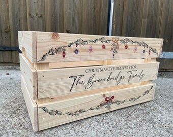 May include: A wooden crate with a Christmas theme. The crate is decorated with a garland of greenery, berries, and ornaments. The text "CHRISTMAS EVE DELIVERY FOR The Brownbridge Family" is printed on the front.