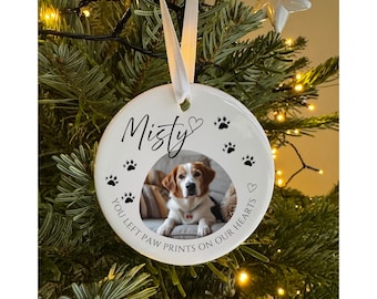 May include: A white ceramic Christmas ornament with a photo of a dog, the name "Misty", paw prints, and the text "YOU LEFT PAW PRINTS ON OUR HEARTS". The ornament hangs from a white ribbon.