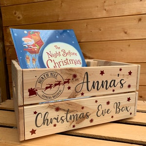 May include: A wooden crate with a red and white "North Pole Express Delivery" stamp, a book titled "The Night Before Christmas", and the text "Anna's Christmas Eve Box" in red lettering with stars.