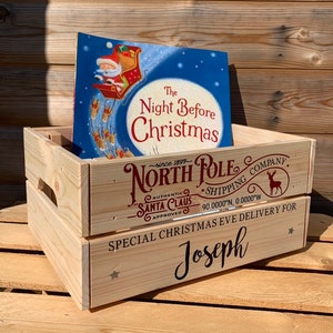 May include: A wooden crate with the words "North Pole Shipping Company" and "Special Christmas Eve Delivery for Joseph" printed on it. The crate is decorated with a reindeer and stars. A book titled "The Night Before Christmas" is sitting inside the crate.