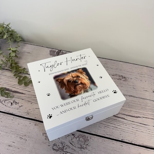 May include: A white wooden box featuring a dog's photo, paw prints, and text. The text says "Taylor Hunter" with dates and "You were our favourite hello... and our hardest goodbye."