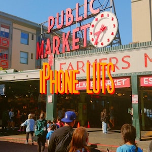Pode incluir: Vista exterior do Pike Place Market em Seattle, com sinalização de néon vermelha que diz "PUBLIC MARKET". Um grande relógio adorna a entrada. As palavras "PHONE LUTS" são sobrepostas na imagem.