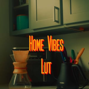 May include: A kitchen counter with a glass coffee maker, a black electric kettle, and a black coffee maker. The text "HOME VIBES LUT" is written in orange and red letters on the counter.