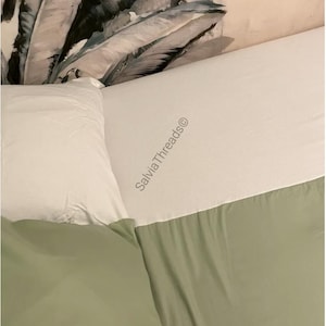Puede incluir: Un juego de cama que incluye una s&aacute;bana encimera blanca con el texto SalviaThreads&copy; impreso, junto con una s&aacute;bana bajera verde salvia y una funda de almohada blanca. La ropa de cama se sit&uacute;a junto a una almohada con estampado bot&aacute;nico.