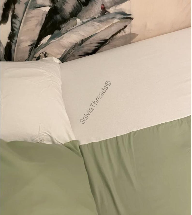 Puede incluir: Un juego de cama que incluye una s&aacute;bana encimera blanca con el texto SalviaThreads&copy; impreso, junto con una s&aacute;bana bajera verde salvia y una funda de almohada blanca. La ropa de cama se sit&uacute;a junto a una almohada con estampado bot&aacute;nico.
