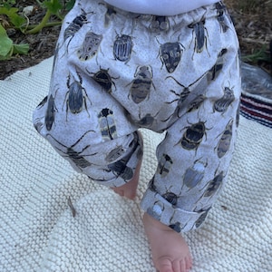 May include: White baby pants with a pattern of colorful beetles. The pants are made of a soft, comfortable fabric and have a relaxed fit.
