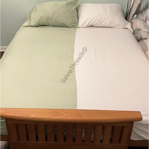 Puede incluir: Una cama con un juego de s&aacute;banas de dos colores, con un lado en verde salvia y el otro en blanco, acompa&ntilde;ado de fundas de almohada a juego. El texto SalviaThreads&copy; est&aacute; impreso en diagonal a trav&eacute;s del centro de la cama.