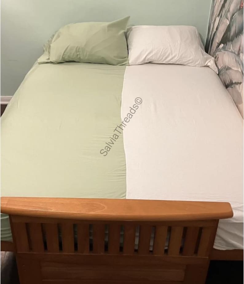 Puede incluir: Una cama con un juego de s&aacute;banas de dos colores, con un lado en verde salvia y el otro en blanco, acompa&ntilde;ado de fundas de almohada a juego. El texto SalviaThreads&copy; est&aacute; impreso en diagonal a trav&eacute;s del centro de la cama.