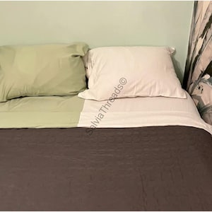 Puede incluir: Un juego de cama que incluye una colcha acolchada de color gris oscuro, una funda de almohada y s&aacute;bana de color verde salvia, y una funda de almohada y s&aacute;bana blancas. El texto SalviaThreads est&aacute; impreso en diagonal sobre la ropa blanca.
