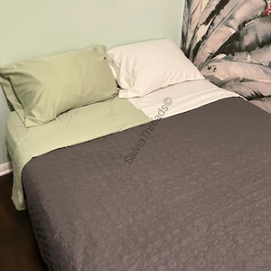 Puede incluir: Una cama con una colcha acolchada de color gris oscuro, una s&aacute;bana encimera de color verde claro, una funda de almohada verde claro a juego y una funda de almohada blanca. El texto SalviaThreads&copy; es visible en el centro.