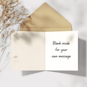Puede incluir: Una tarjeta de felicitaci&oacute;n abierta con un interior en blanco, acompa&ntilde;ada de un sobre marr&oacute;n. El lado derecho de la tarjeta presenta el texto "Blank inside for your own message" en escritura negra. Elementos florales secos son visibles.