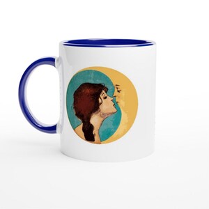 Op de afbeelding: Witte keramische mok met een blauwe handgreep en rand. De mok heeft een vintage illustratie van twee figuren in profiel, tegen een turquoise en gele achtergrond. Het ontwerp roept een hemels thema op.