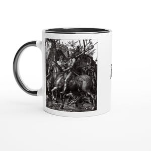 Könnte beinhalten: Weißer Keramikbecher mit schwarzem Henkel und Rand. Der Becher zeigt eine detaillierte Schwarz-Weiß-Illustration eines Ritters zu Pferd, umgeben von anderen Figuren und Tieren. Das Design erinnert an einen klassischen Stich.
