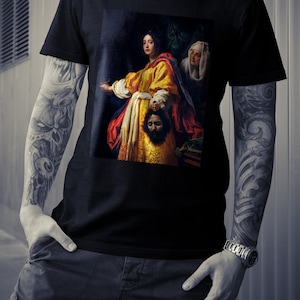 May include: A black t-shirt with a painting of a woman holding a severed head. The woman is wearing a yellow and red dress and a white head covering. The painting is in a dark, dramatic style.