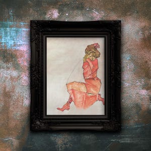 Könnte beinhalten: Gerahmtes Kunstwerk mit einem Aquarellgemälde einer sitzenden Figur in Rot- und Orangetönen. Die Figur hat den Kopf in den Händen. Das Kunstwerk befindet sich in einem schwarzen, verzierten Rahmen.