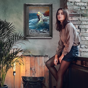 May include: A woman wearing a brown jumper and black shorts sits on a windowsill in front of a brick wall. A framed painting of a mermaid in the ocean hangs on the wall behind her.