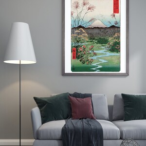 May include: A framed print of a Japanese landscape painting featuring Mount Fuji, a winding river, and red flowers. The painting is in a gray frame with a white mat.