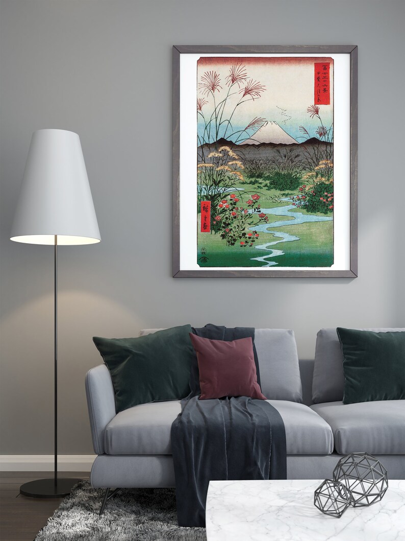 May include: A framed print of a Japanese landscape painting featuring Mount Fuji, a winding river, and red flowers. The painting is in a gray frame with a white mat.