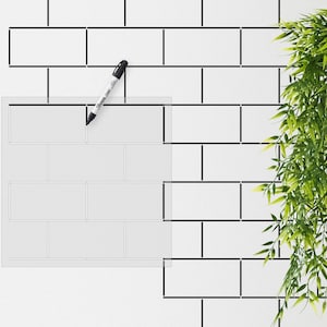 Puede incluir: Una pared de azulejos blancos con líneas de lechada negras. Una plantilla transparente se coloca sobre los azulejos, delineando un patrón de cuadrícula. Un marcador negro está sobre la pared.