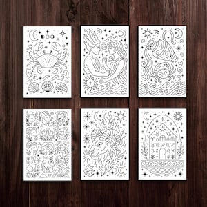 May include: Six black and white art prints featuring zodiac illustrations. Each print showcases detailed line art of astrological symbols, including a crab, figures, and an ram. The prints are arranged on a dark wood surface.