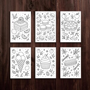 May include: Six black and white dessert illustrations on white cards. The illustrations include a cake with a lemon slice, macarons, a pie, ice cream in a cone, a cupcake, and an &eacute;clair. Each card has a decorative border of leaves and other elements.