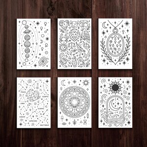 May include: Six white rectangular cards with black line art illustrations of celestial and astrological themes. The cards feature planets, constellations, zodiac symbols, and decorative elements. The cards are arranged on a dark wood surface.