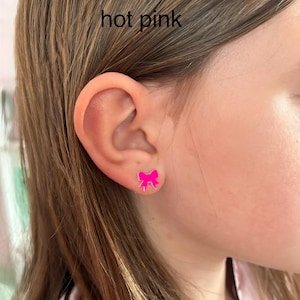May include: Hot pink bow-shaped stud earrings. The earrings are a bright, solid pink color and are worn on the ear. The text "hot pink" is visible in the image.