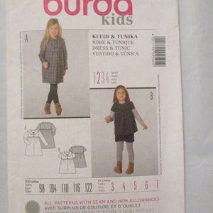 May include: Burda Kids sewing pattern 9504 for a dress and tunic. The pattern includes sizes 98 to 122 cm and 3 to 7 US sizes. The pattern includes seam and hem allowances. The pattern is for a plaid dress and a solid black tunic.