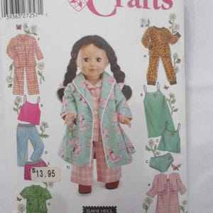 May include: Simplicity Crafts pattern 5276 for doll clothing. The envelope features a doll with long dark braided hair wearing a light green floral robe over pink plaid pajamas. Illustrations show various pajama sets, including leopard print, solid green, and pink plaid options.