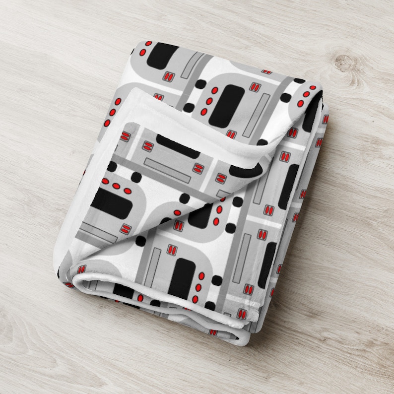 May include: A white fleece blanket with a repeating pattern of gray and black ovens with red knobs.