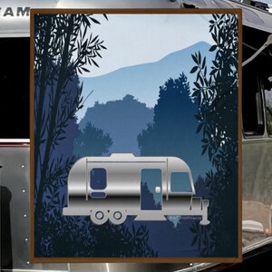 May include: A silver Airstream trailer is parked in a forest setting with blue mountains in the background. The trailer is surrounded by trees with dark blue leaves.