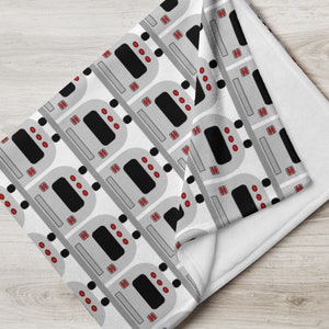 May include: A white fleece blanket with a repeating pattern of gray and black subway trains with red lights. The blanket is folded in half, showing the white fleece backing.